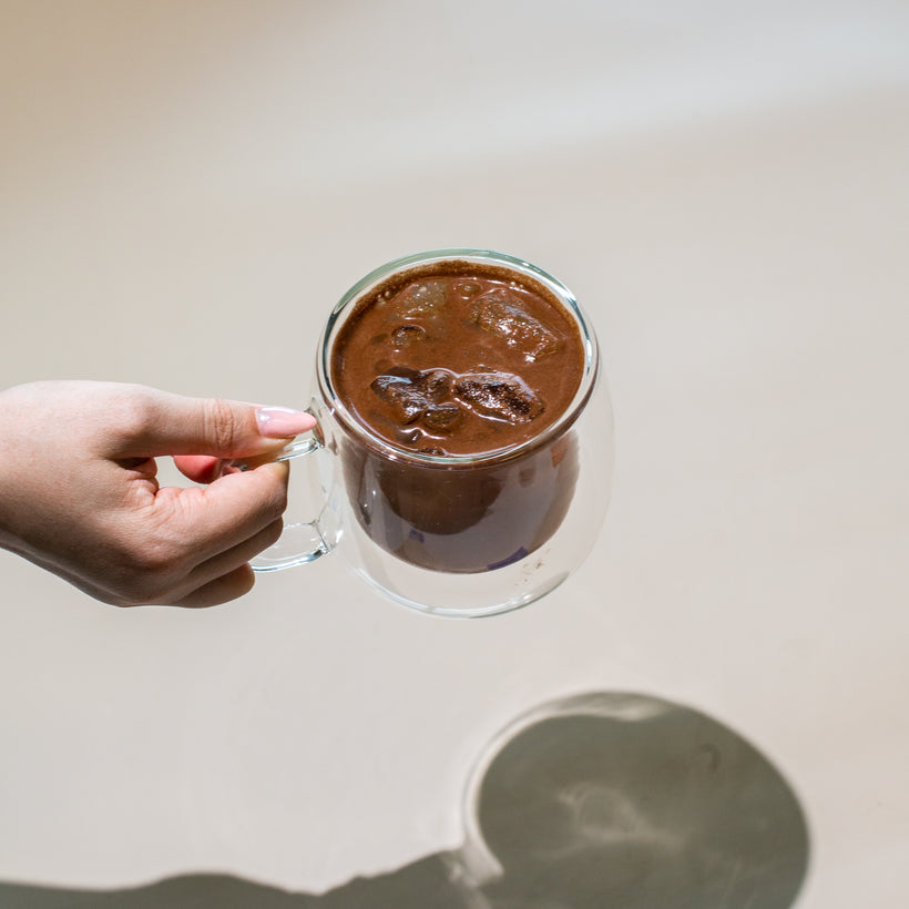 Hand holding a glass mug of iced chocolate drink.